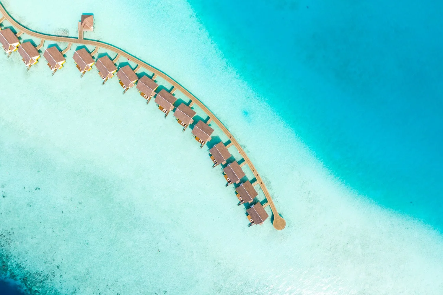 Overwater villas curve around the turquoise lagoon at SAii Lagoon Maldives